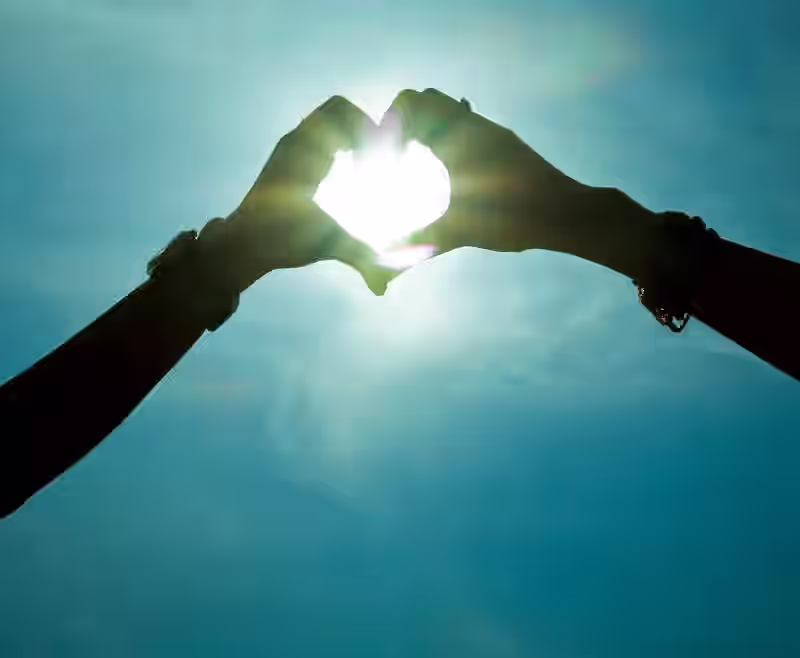 Corazón formado con la manos con el sol de fondo